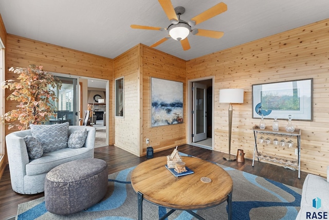 living room with ceiling fan, wooden walls, and dark hardwood / wood-style flooring