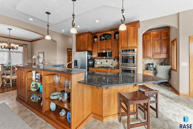 kitchen featuring a breakfast bar area, dark stone countertops, hanging light fixtures, stainless steel appliances, and a large island with sink