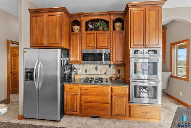 kitchen with tasteful backsplash, a textured ceiling, dark stone countertops, light tile patterned floors, and stainless steel appliances