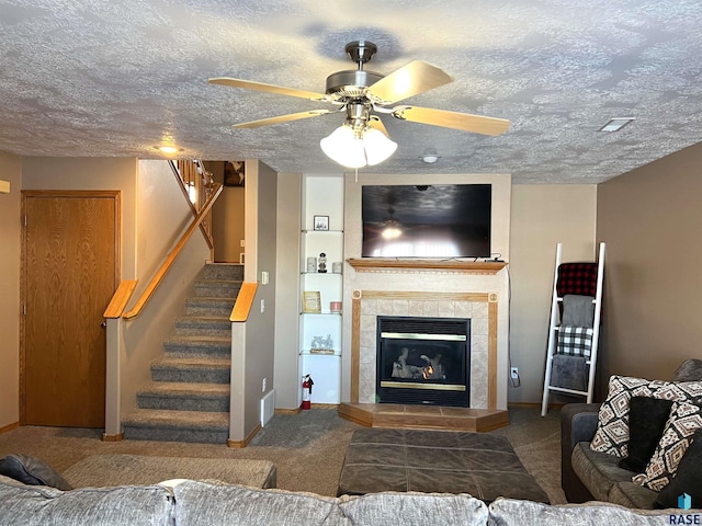 carpeted living room with a tiled fireplace, ceiling fan, and a textured ceiling