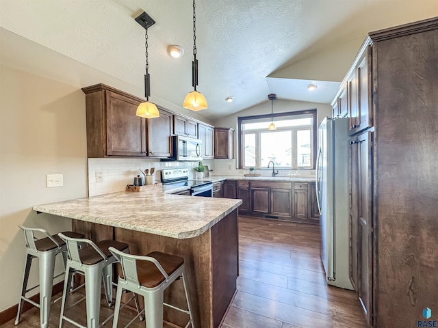 kitchen featuring stainless steel appliances, lofted ceiling, sink, and decorative light fixtures