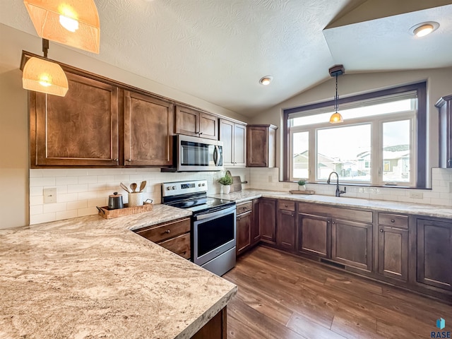 kitchen with lofted ceiling, hanging light fixtures, appliances with stainless steel finishes, dark hardwood / wood-style flooring, and light stone countertops