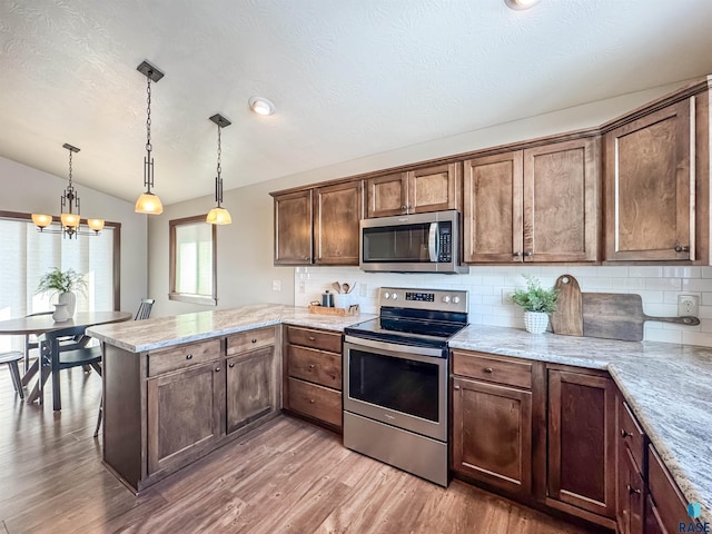 kitchen featuring vaulted ceiling, appliances with stainless steel finishes, hardwood / wood-style floors, pendant lighting, and kitchen peninsula