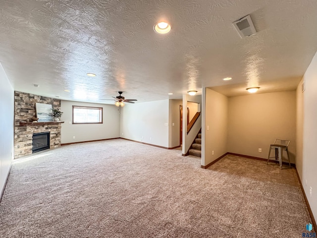 unfurnished living room with ceiling fan, a stone fireplace, carpet floors, and a textured ceiling