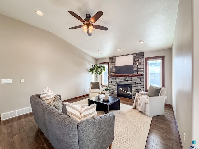 living room featuring a stone fireplace, dark wood-type flooring, ceiling fan, and vaulted ceiling