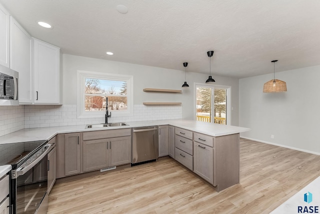 kitchen with sink, gray cabinetry, kitchen peninsula, pendant lighting, and stainless steel appliances