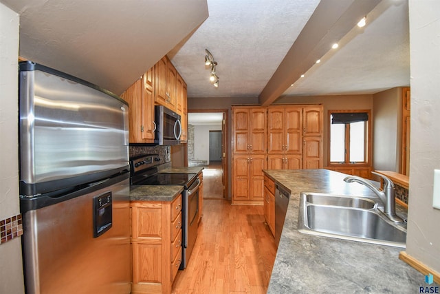 kitchen featuring sink, stainless steel appliances, light hardwood / wood-style floors, a textured ceiling, and decorative backsplash