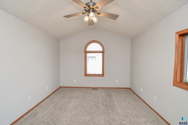 carpeted spare room featuring a textured ceiling, vaulted ceiling, and ceiling fan