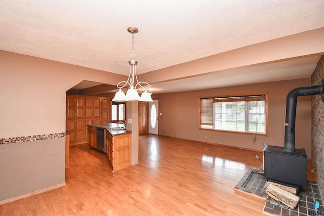 kitchen with pendant lighting, sink, light hardwood / wood-style flooring, stainless steel dishwasher, and a wood stove