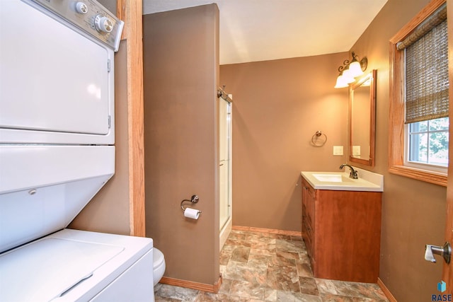 bathroom featuring vanity, stacked washer / drying machine, toilet, and an enclosed shower