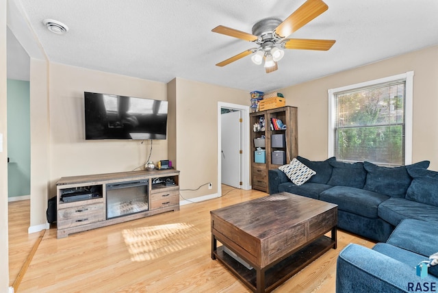 living room with ceiling fan, light hardwood / wood-style floors, and a textured ceiling