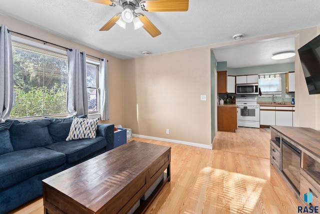 living room featuring ceiling fan, sink, light hardwood / wood-style flooring, and a textured ceiling