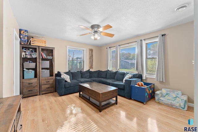 living room with ceiling fan, a textured ceiling, light hardwood / wood-style flooring, and a healthy amount of sunlight