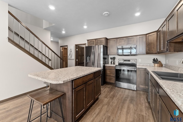 kitchen with a kitchen island, wood-type flooring, a breakfast bar area, dark brown cabinetry, and stainless steel appliances