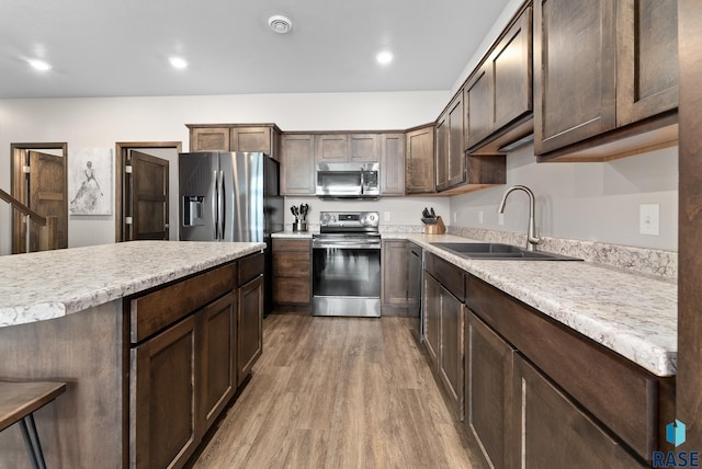 kitchen featuring appliances with stainless steel finishes, sink, dark brown cabinets, and light wood-type flooring