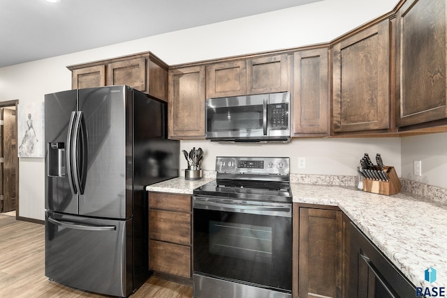 kitchen featuring light stone counters, dark brown cabinetry, appliances with stainless steel finishes, and light hardwood / wood-style flooring