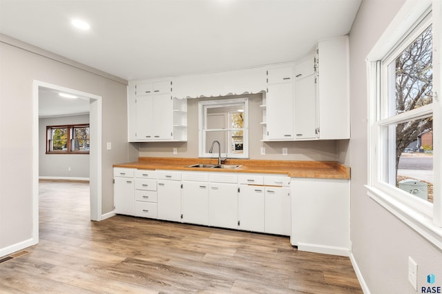 kitchen with butcher block counters, sink, light hardwood / wood-style floors, and white cabinets