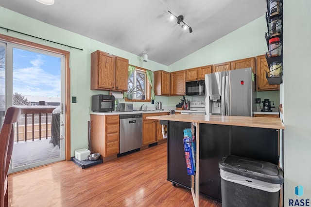 kitchen featuring lofted ceiling, sink, rail lighting, appliances with stainless steel finishes, and light wood-type flooring