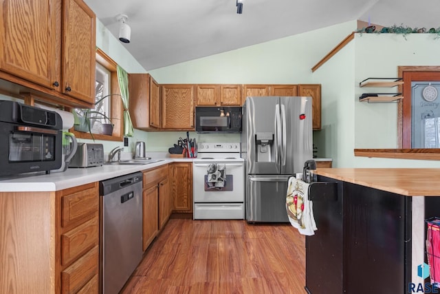 kitchen with vaulted ceiling, appliances with stainless steel finishes, sink, and light hardwood / wood-style floors