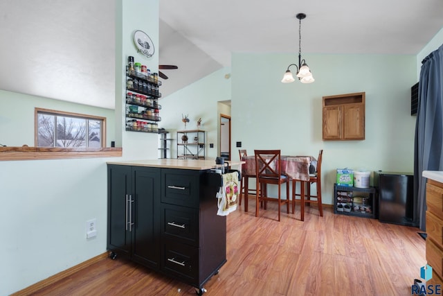 kitchen featuring vaulted ceiling, decorative light fixtures, a notable chandelier, kitchen peninsula, and light hardwood / wood-style flooring