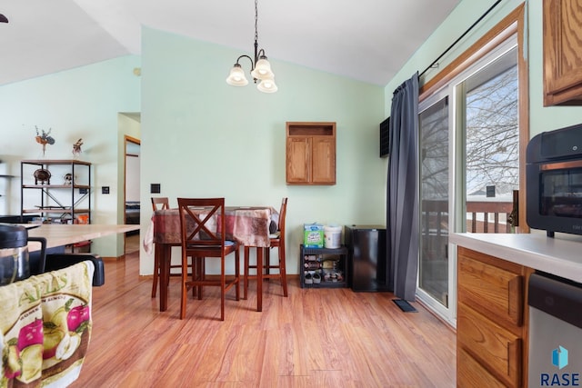 dining room with lofted ceiling, an inviting chandelier, and light wood-type flooring