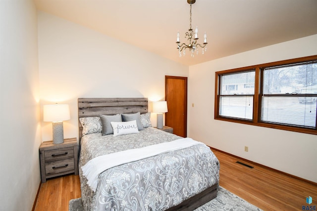 bedroom with lofted ceiling, light hardwood / wood-style floors, and an inviting chandelier