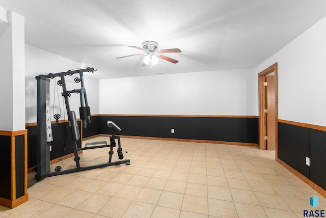 exercise area with ceiling fan, a textured ceiling, and wooden walls