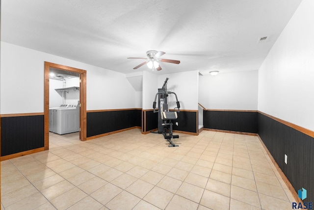 workout area with ceiling fan, wooden walls, washing machine and clothes dryer, a textured ceiling, and light tile patterned flooring