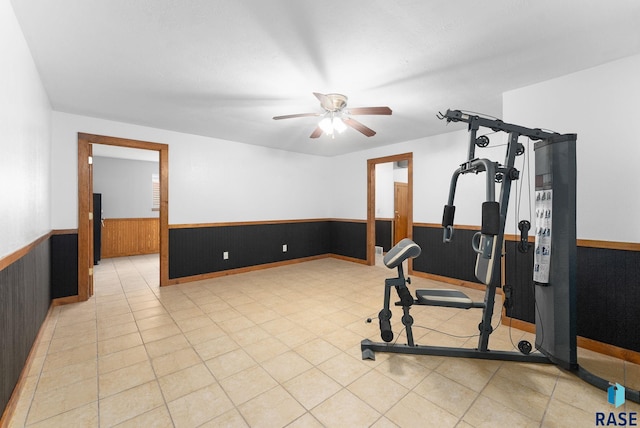 exercise room with light tile patterned floors, wooden walls, and ceiling fan