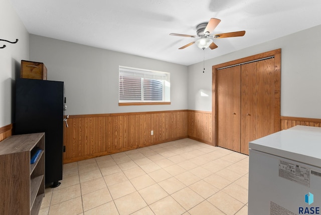 kitchen featuring light tile patterned flooring, ceiling fan, wooden walls, and black fridge