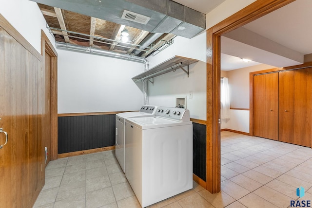 washroom featuring wooden walls, washing machine and dryer, and light tile patterned floors