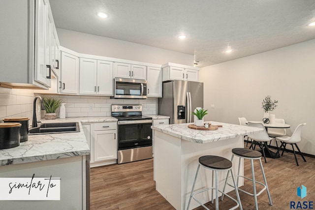 kitchen featuring a kitchen island, appliances with stainless steel finishes, white cabinetry, sink, and a kitchen breakfast bar