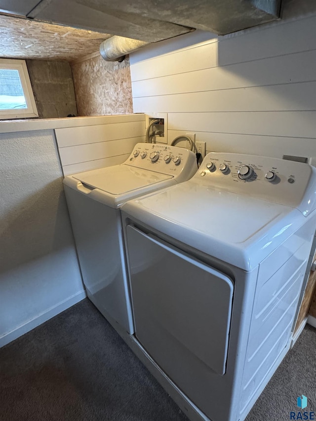 clothes washing area with wooden walls, washing machine and dryer, and dark colored carpet