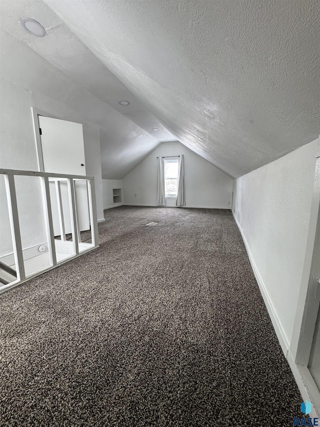 additional living space with carpet floors, vaulted ceiling, and a textured ceiling