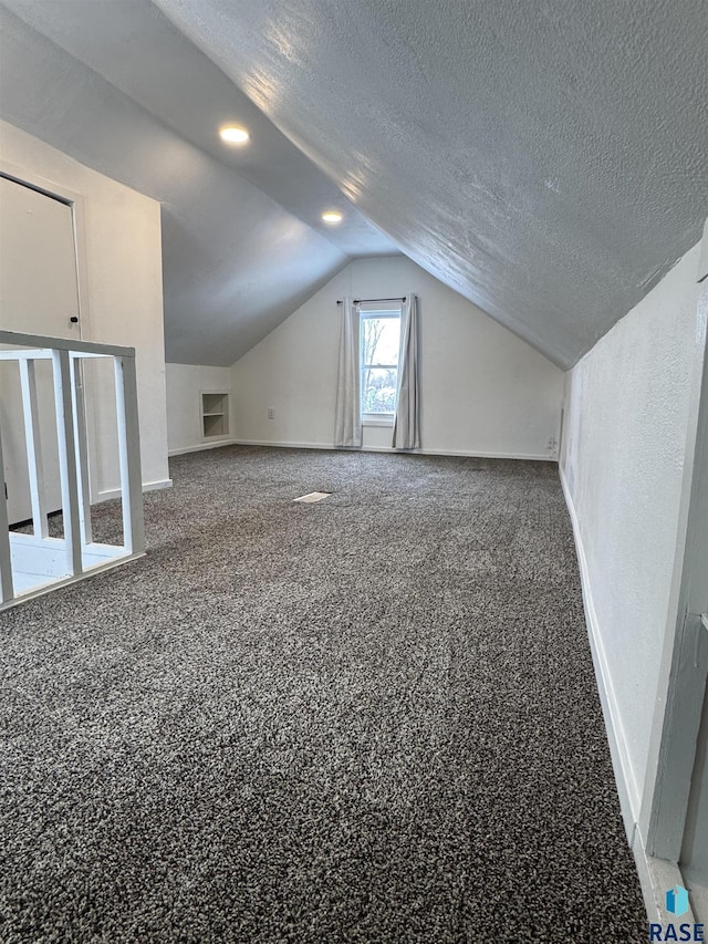 additional living space featuring carpet floors, vaulted ceiling, and a textured ceiling