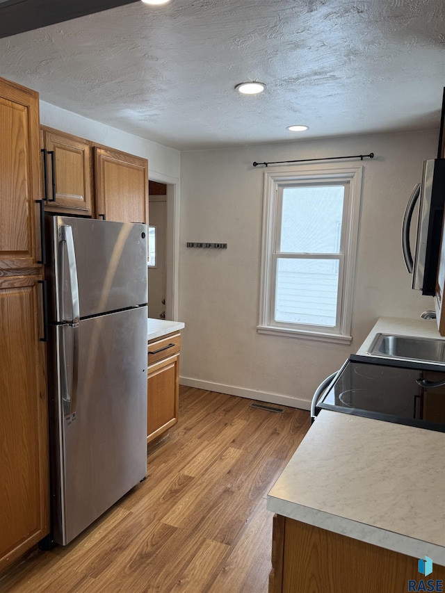 kitchen with sink, light wood-type flooring, a textured ceiling, and appliances with stainless steel finishes