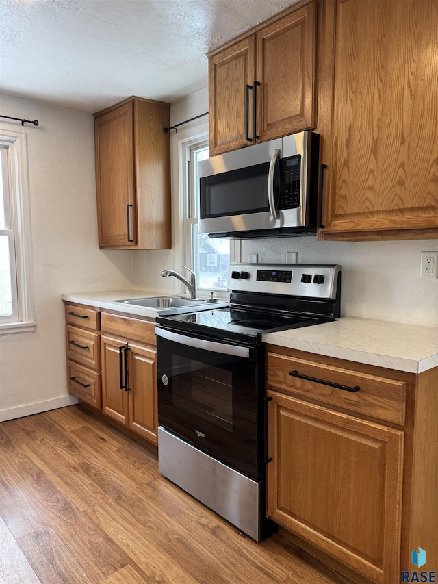 kitchen featuring appliances with stainless steel finishes, a healthy amount of sunlight, sink, and light hardwood / wood-style flooring