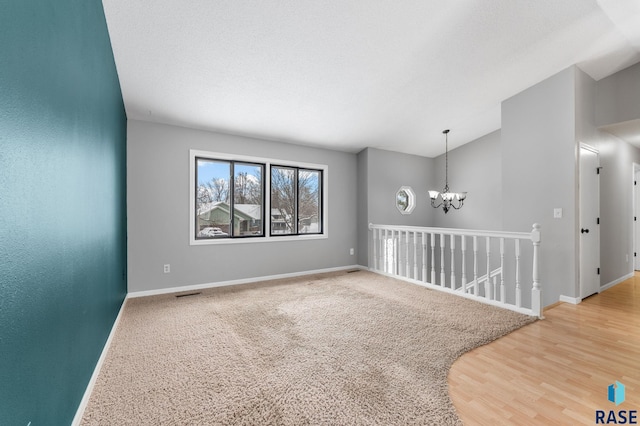 empty room featuring vaulted ceiling, wood-type flooring, a textured ceiling, and a chandelier