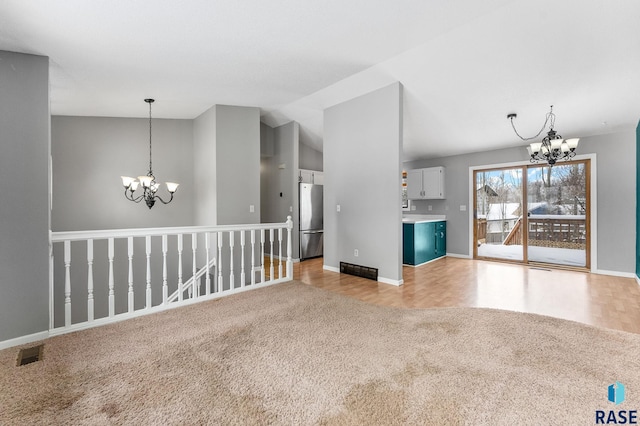 unfurnished living room with light colored carpet, vaulted ceiling, and a notable chandelier