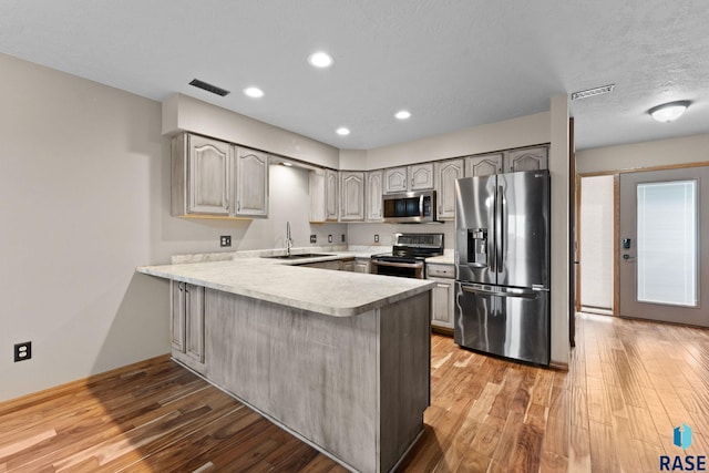 kitchen featuring appliances with stainless steel finishes, sink, kitchen peninsula, and light hardwood / wood-style floors