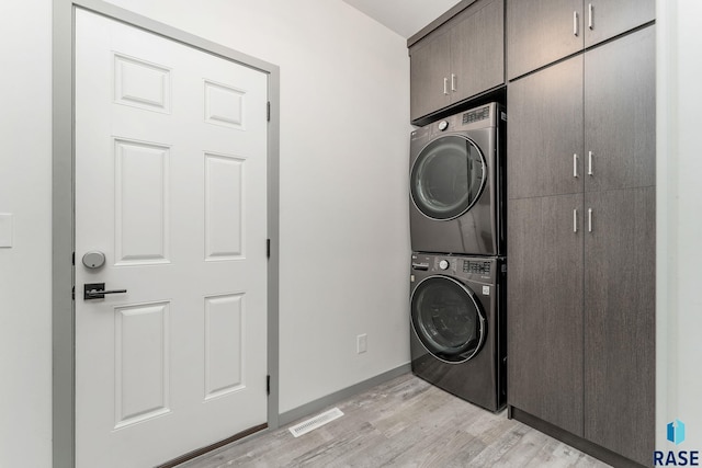 laundry room featuring stacked washer / drying machine, cabinets, and light wood-type flooring