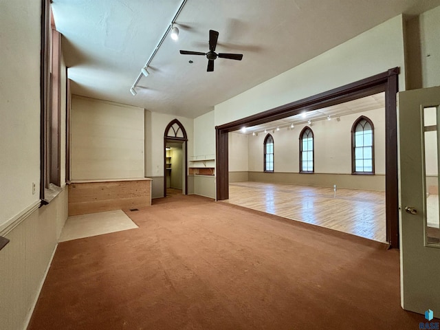 unfurnished living room featuring ceiling fan, rail lighting, and carpet