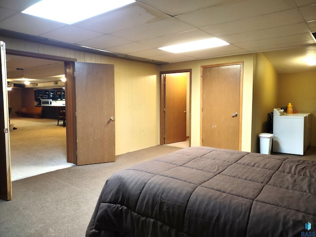 carpeted bedroom featuring a drop ceiling, washer / clothes dryer, and wood walls