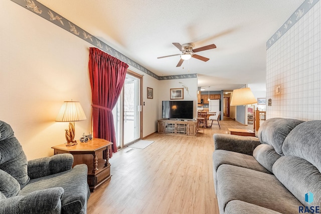 living room with ceiling fan, a textured ceiling, and light wood-type flooring