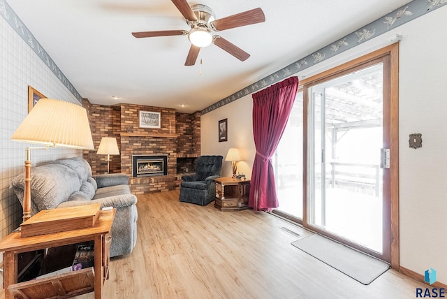 living room with ceiling fan, plenty of natural light, a fireplace, and light hardwood / wood-style flooring