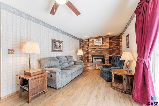 living room featuring ceiling fan, a brick fireplace, and light hardwood / wood-style flooring