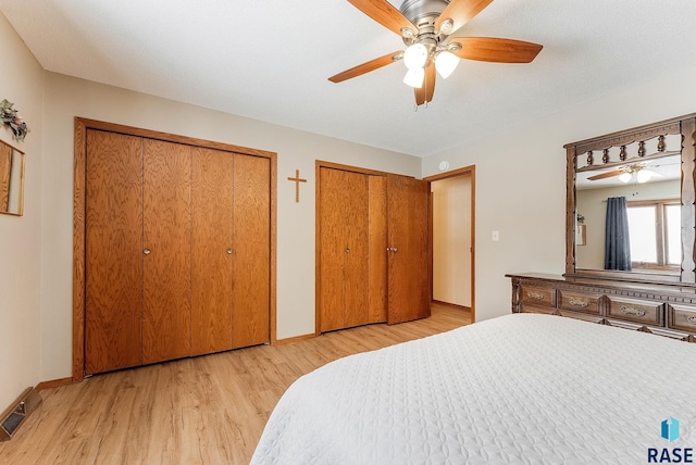 bedroom with two closets, light hardwood / wood-style floors, and ceiling fan