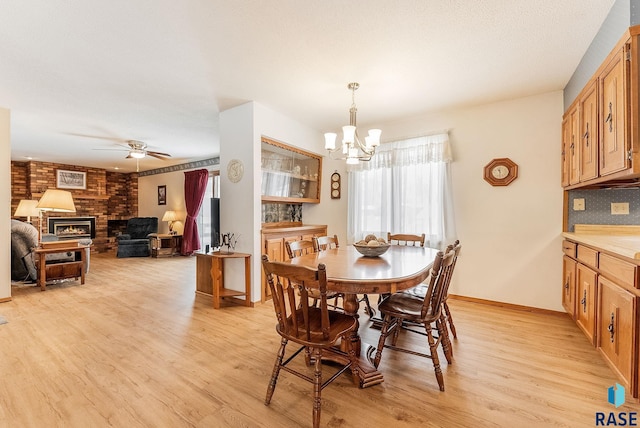 dining space with a brick fireplace, ceiling fan with notable chandelier, and light hardwood / wood-style flooring