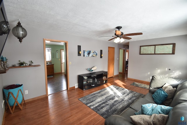 living room with a textured ceiling, ceiling fan, wood finished floors, and baseboards