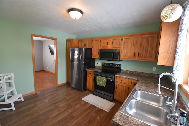 kitchen featuring brown cabinetry, dark countertops, hanging light fixtures, black appliances, and a sink